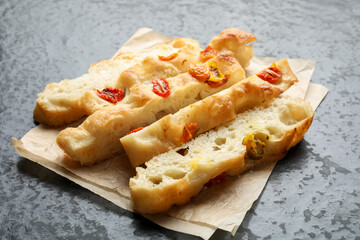 Pieces of delicious focaccia with tomatoes on gray textured table, closeup