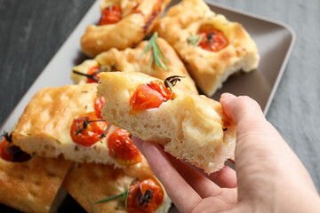 Woman holding piece of delicious focaccia with tomatoes and spices at table, closeup