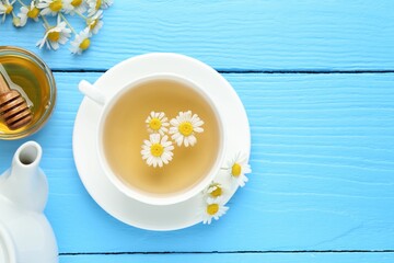 Delicious chamomile tea in cup, fresh flowers and honey on light blue wooden table, flat lay. Space for text