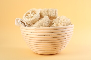 Different loofah sponges in bowl on beige background, closeup