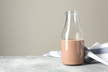 Tasty chocolate milk in glass bottle on grey table, space for text