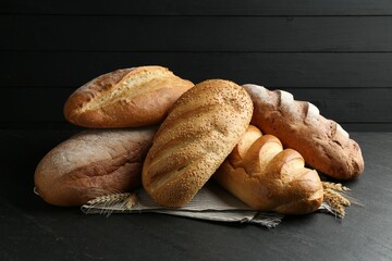 Many different loaves of bread and spikes on black textured table