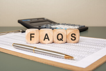 Wooden cubes with word FAQS on financial spreadsheet.