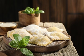 Uncooked ravioli and basil on wooden table, closeup. Space for text