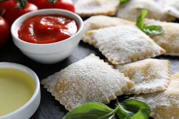 Uncooked ravioli, sauce, tomatoes and basil on black table, closeup