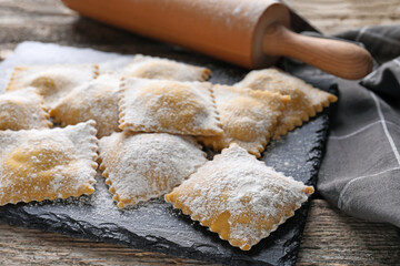 Uncooked ravioli and rolling pin on wooden table, closeup