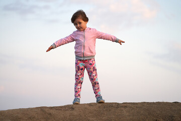 A little girl with her arms spread apart stands on a dais against the sky. Her hair is ruffled by the wind. Copy space.