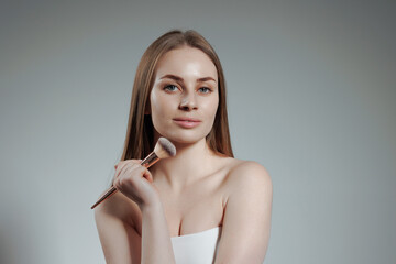 Model showcasing makeup application techniques with a brush in a studio setting during a photoshoot