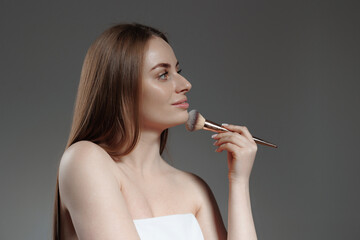 Obraz premium Model applies makeup with a brush while posing against a neutral background in a fashion studio setting