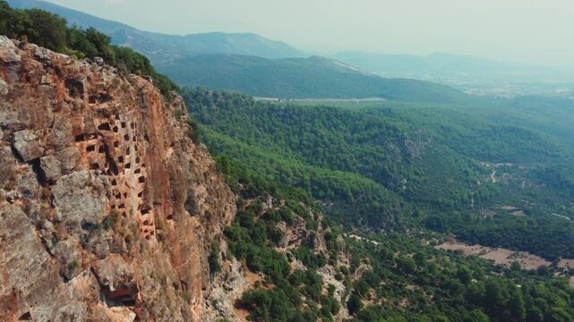 Remains of an ancient Lycian rock necropolis in the city of Pinara in Turkey. A rock with carved tombs. Lycian rock tombs overlooking the ancient Lycian city of Pinara from the air. Drone. 4К