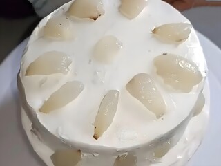 A beautifully decorated lychee cake topped with fresh cream and juicy lychee slices. Ideal for food photography, dessert menus, baking blogs, and culinary designs.
