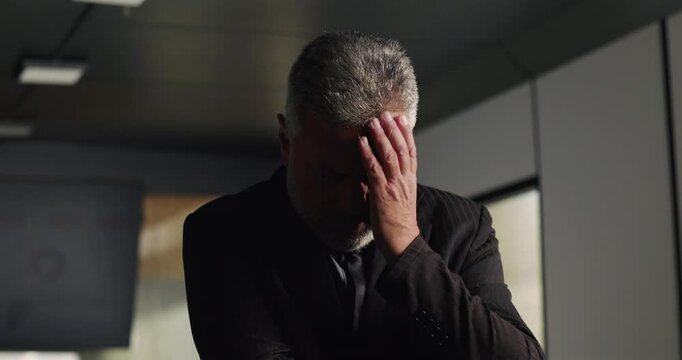 Frustrated businessman holding back emotion while running hand through hair in tense office meeting during corporate setback