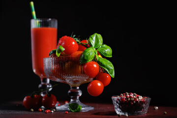Tomato juice and ripe cherry tomatoes in a glass bowl with basil leaves on a textured dark background