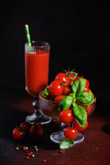 Fresh cherry tomatoes and basil in glass bowl with tall glass of tomato juice and pepper mix
