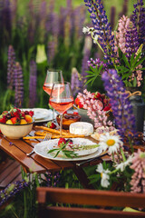 Romantic surprise, marriage proposal. Elegant decoration. Private wedding party for two, table set with floral decor, chandelier, fruits, wine in field or meadow. Summer, sunset, golden hour