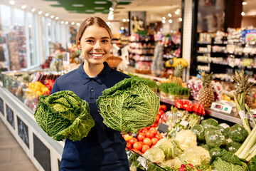 Smiling grocery store employee holding fresh cabbage heads