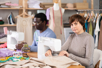Working in sewing workshop - man and a woman working at sewing machines, creating new clothes