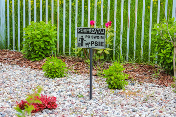 Warning Sign Posted in Decorative Garden Area with White Gravel, Green Shrubs and Vertical Metal...