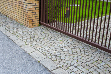 Cobblestone Pavement Meeting Metal Gate Entrance with Green Lawn Beyond Residential Boundary