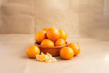 Fresh Oranges in Ceramic Bowl with Peeled Segments on Brown Paper Background