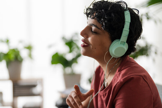 A woman with headphones is enjoying music. She's relaxing and letting the sound wash over her, maybe to de-stress or simply enjoy her favorite tunes.