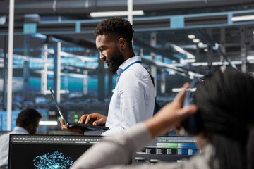 Data center specialist using AI deep learning algorithms on laptop to analyze large datasets. Man...