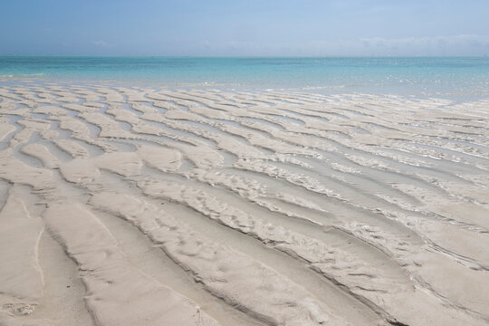 Gentle ripples on the soft white sand. A shallow sandbank near Mnemba Island, Zanzibar, Tanzania. Sunlit shallow waters close to the coral reef on the northeastern coast of Zanzibar.