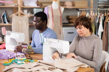 Two dedicated fashion designers, woman and man, sewing custom garments at machines, focusing on precision and detail, bringing creative visions to life in collaborative studio filled with inspiration