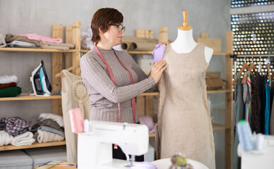 Female dressmaker trying on a new dress on a mannequin in a sewing workshop