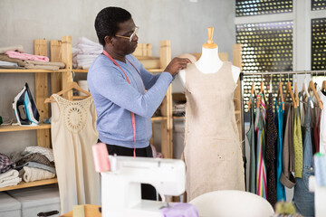 In workshop, African American male employee dressmaker works with mannequin and future dress. Woman...