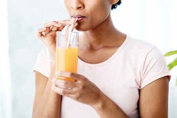 Fototapeta premium Pretty black woman drinking fresh orange juice at home, panorama. Slim African American lady having tasty fruit beverage indoors. Healthy living and detox concept