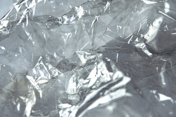 Crinkled cellophane texture with glossy surfaces in shades of grey and translucent highlights creating an abstract