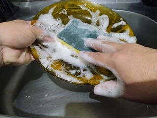 Hand with a sponge washing a plate.