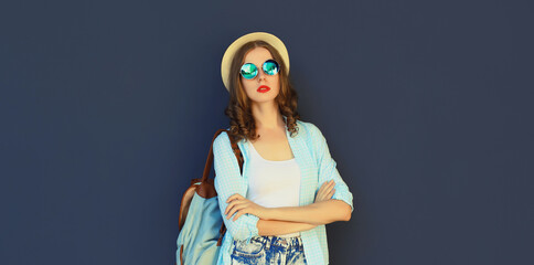 Portrait stylish modern young woman in summer tourist hat with backpack posing on black background