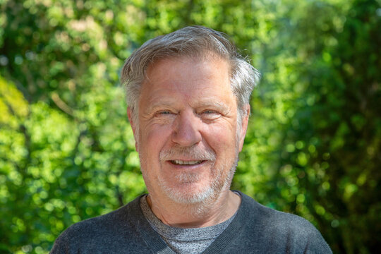 portrait of friendly handsome senior man with grey hair with green garden in background