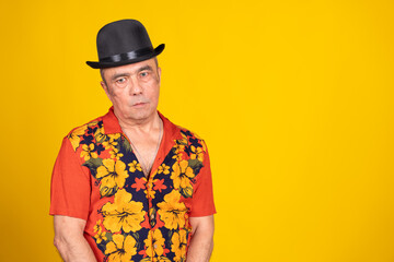 Senior man wearing hawaiian shirt and bowler hat on yellow background