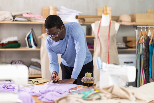 Male tailor cutting fabric with scissors while working in sewing workshop