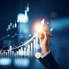 Realistic image of a hand drawing an upward arrow on a transparent screen, with bright light effects, financial charts overlay, and symbols of profit and business growth.