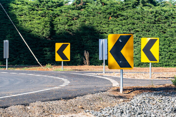 Curved rural road with multiple chevron alignment signs in Victoria, Australia, guiding drivers safely around the bend. Concept of road safety, directional signage and  transport infrastructure 