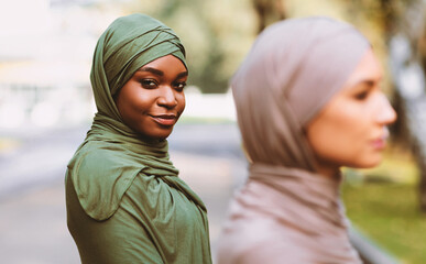 Fototapeta premium Two Diverse Muslim Women Posing Wearing Traditional Hijab Headscarf Looking At Camera Standing Outdoors. Diversity And Unity Of Islamic Females Concept. Selective Focus