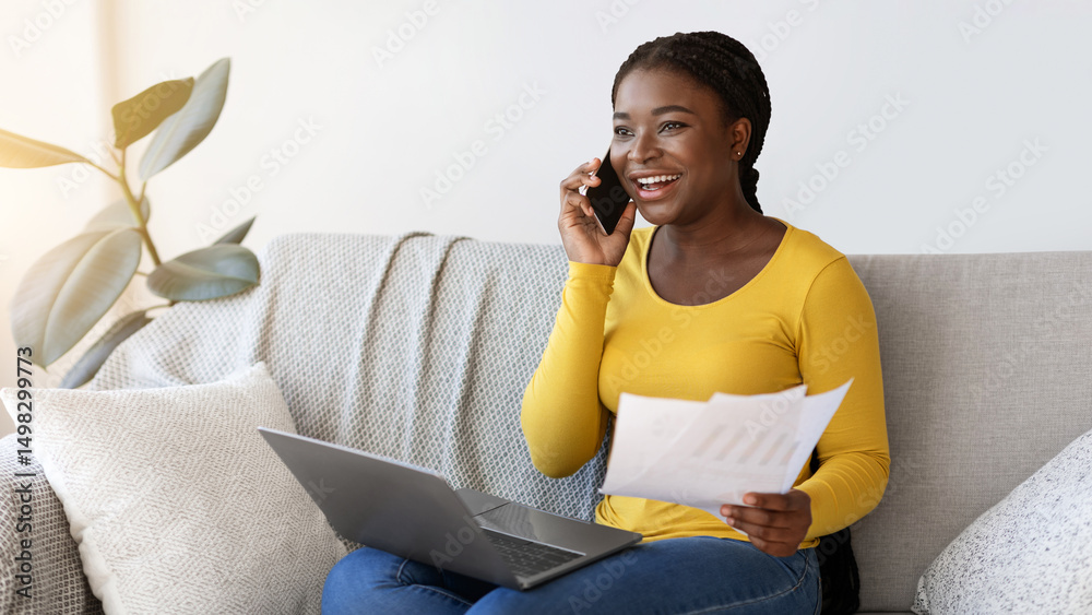 Aufkleber Work From Home. Smiling Black Freelancer Lady Talking On Cellphone While Working With Papers And Laptop On Couch In Living Room, African Lady Enjoying Remote Job And Mobile Communication, Copy Space