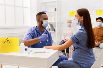 Fototapeta premium Successful Coronavirus Vaccination. Doctor In Face Mask Gesturing Thumbs-Up To Vaccinated Against Corona Virus Female Patient Sitting In Hospital. Covid Vaccine Injection And Immunization Campaign