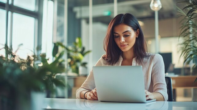 Focused young professional working diligently on her laptop in modern office