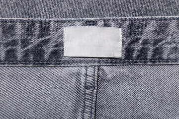 Clothing label on gray jeans waistband, white tag on textile, inside out denim fabric