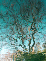 Blue water reflex background. Abstract reflection and abstract inspection elements in water. Nature elements distorted in the river. Rippled trees water texture. Graphic water surface.