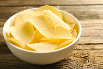 Tasty potato chips in bowl on wooden table, closeup