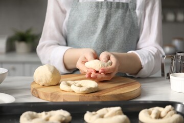 Woman shaping pretzels at table in kitchen, closeup