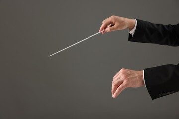 Professional conductor with baton on grey background, closeup. Space for text