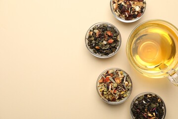 Delicious herbal tea in glass cup and dry leaves on beige background, flat lay. Space for text