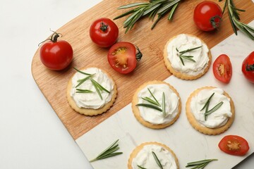 Tasty crackers with cream cheese, rosemary and tomatoes on white table, top view